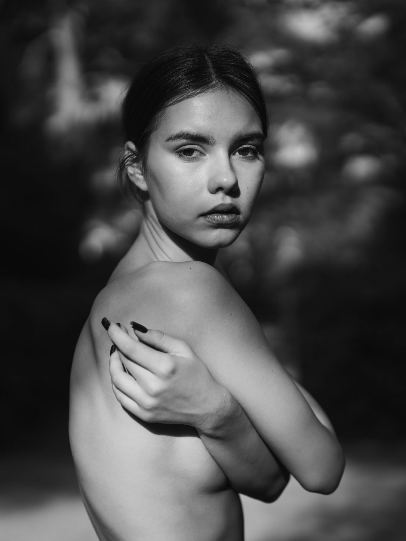 Nude model from behind with hand on her shoulder looking back in a garden, black and white – artistic photography by VicmanArt