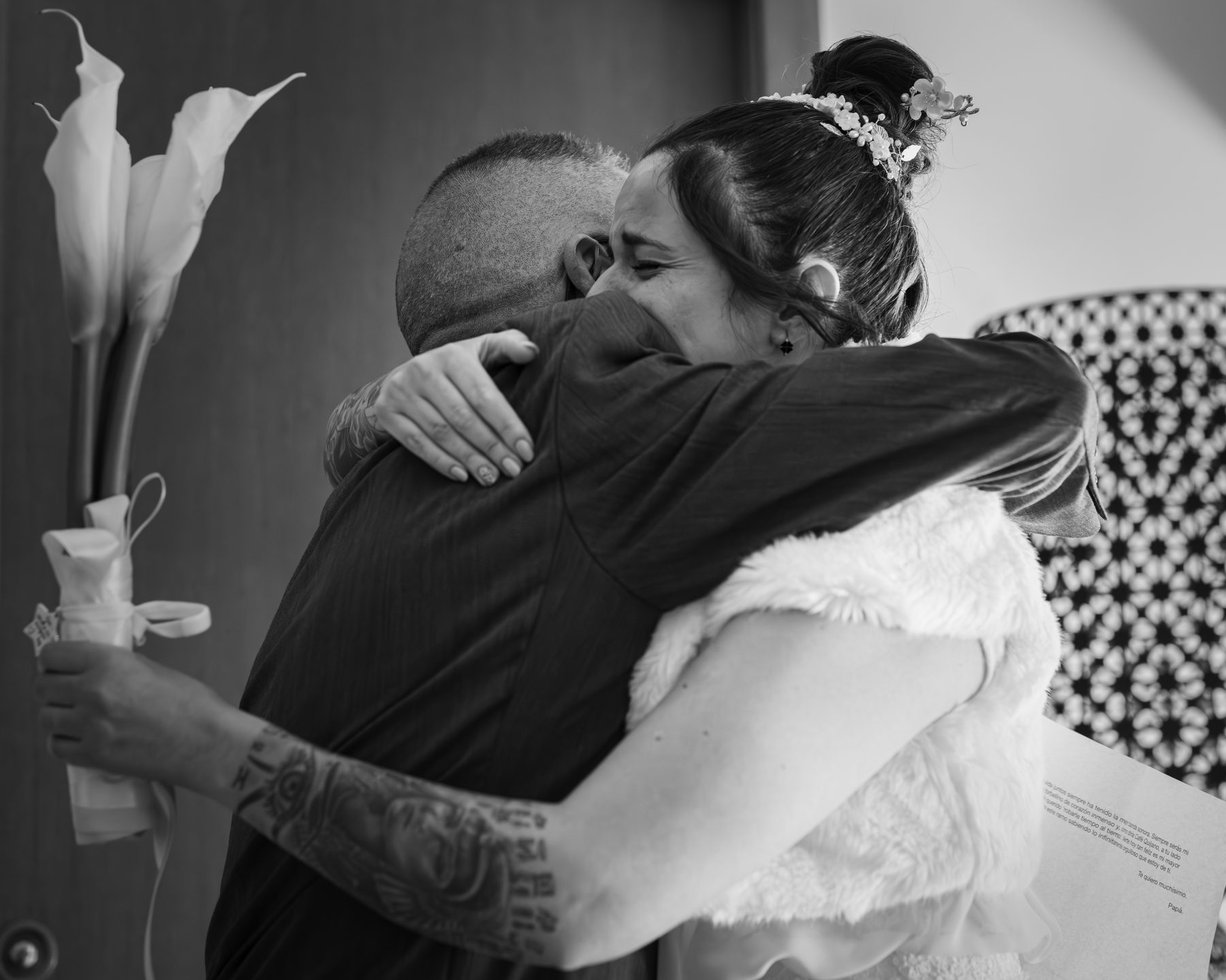 Novia abrazando emocionada a familiar sosteniendo un ramo de lirios blancos, blanco y negro – fotografía de bodas por VicmanArt