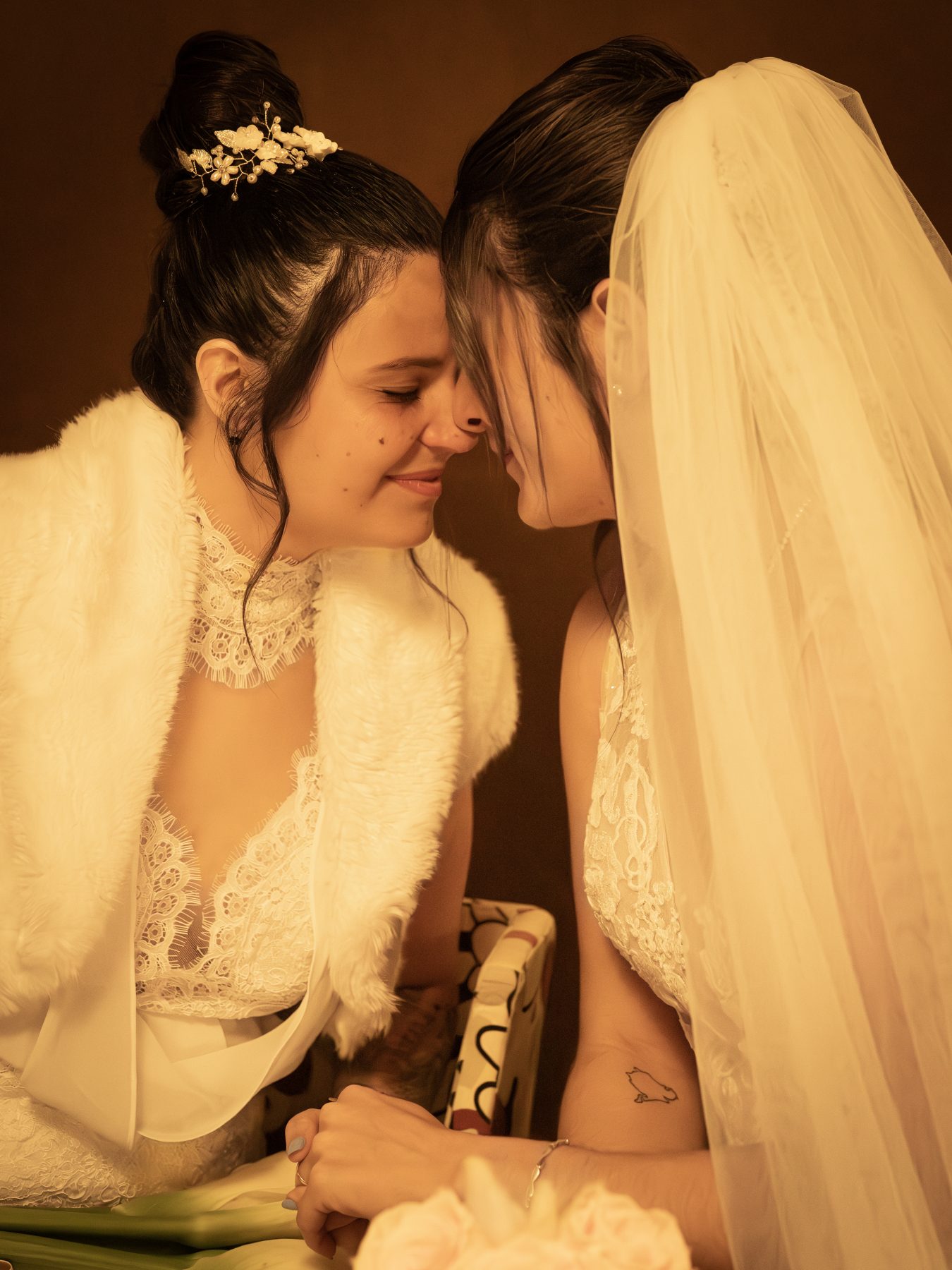 Las dos novias con frentes juntas en íntimo momento antes de la ceremonia, tonos dorados cálidos – fotografía de bodas por VicmanArt