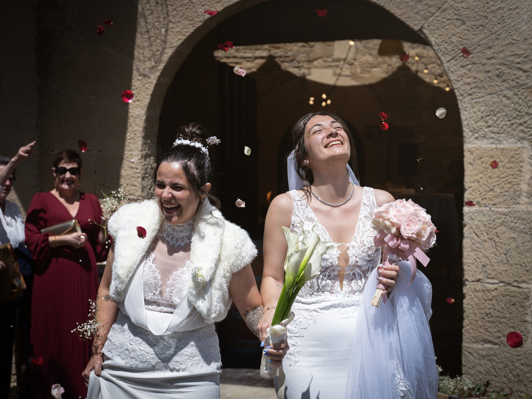 Las dos novias saliendo de la ceremonia bajo lluvia de pétalos de rosa en Barcelona – fotografía de bodas por VicmanArt