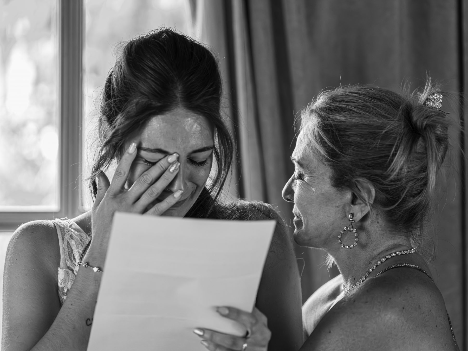 Novia emocionada llorando al leer una carta mientras la madre la consuela, blanco y negro – fotografía de bodas por VicmanArt