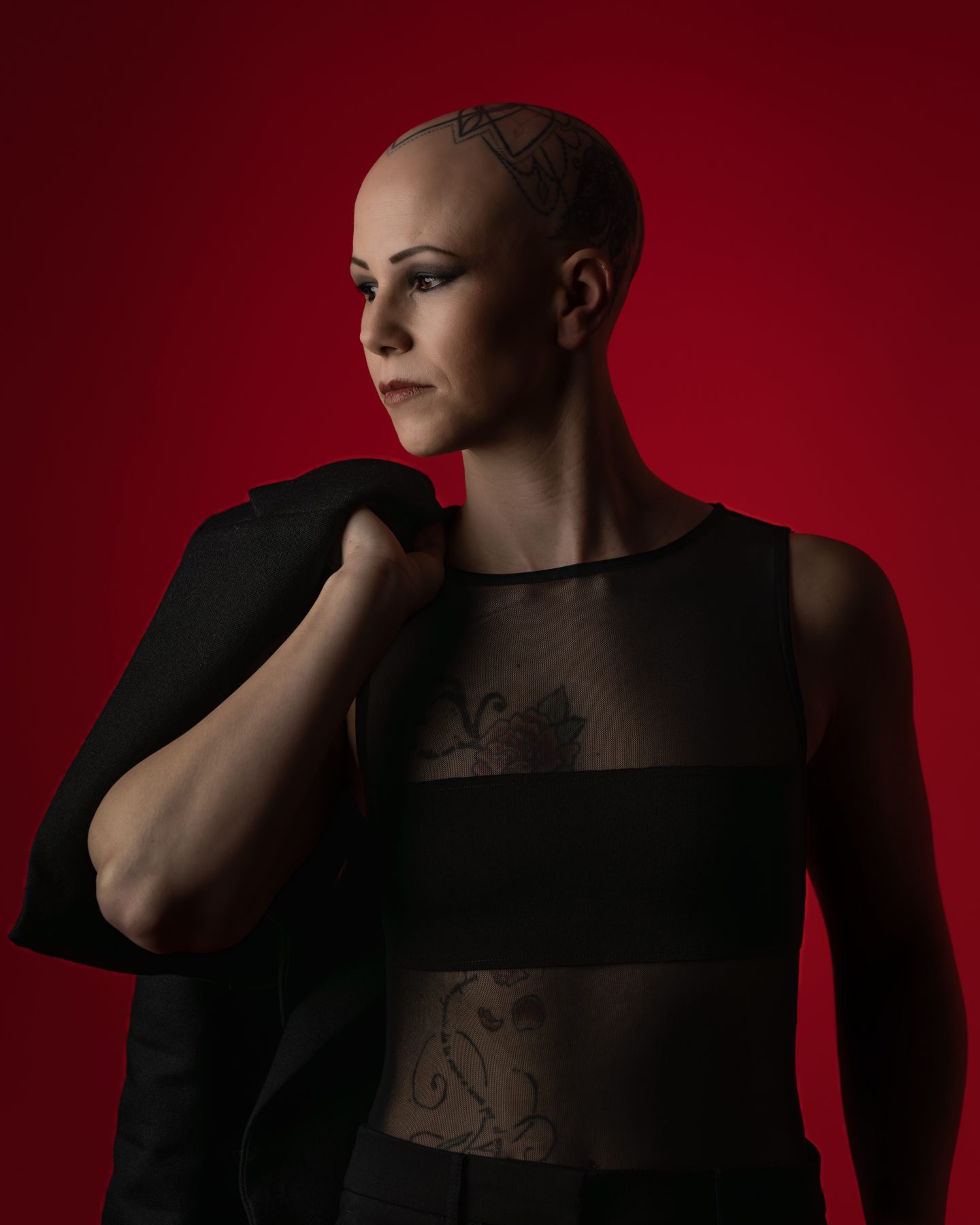 Modelo con cabeza rapada en top de tul negro con blazer al hombro, fondo rojo – fotografía editorial de moda por VicmanArt