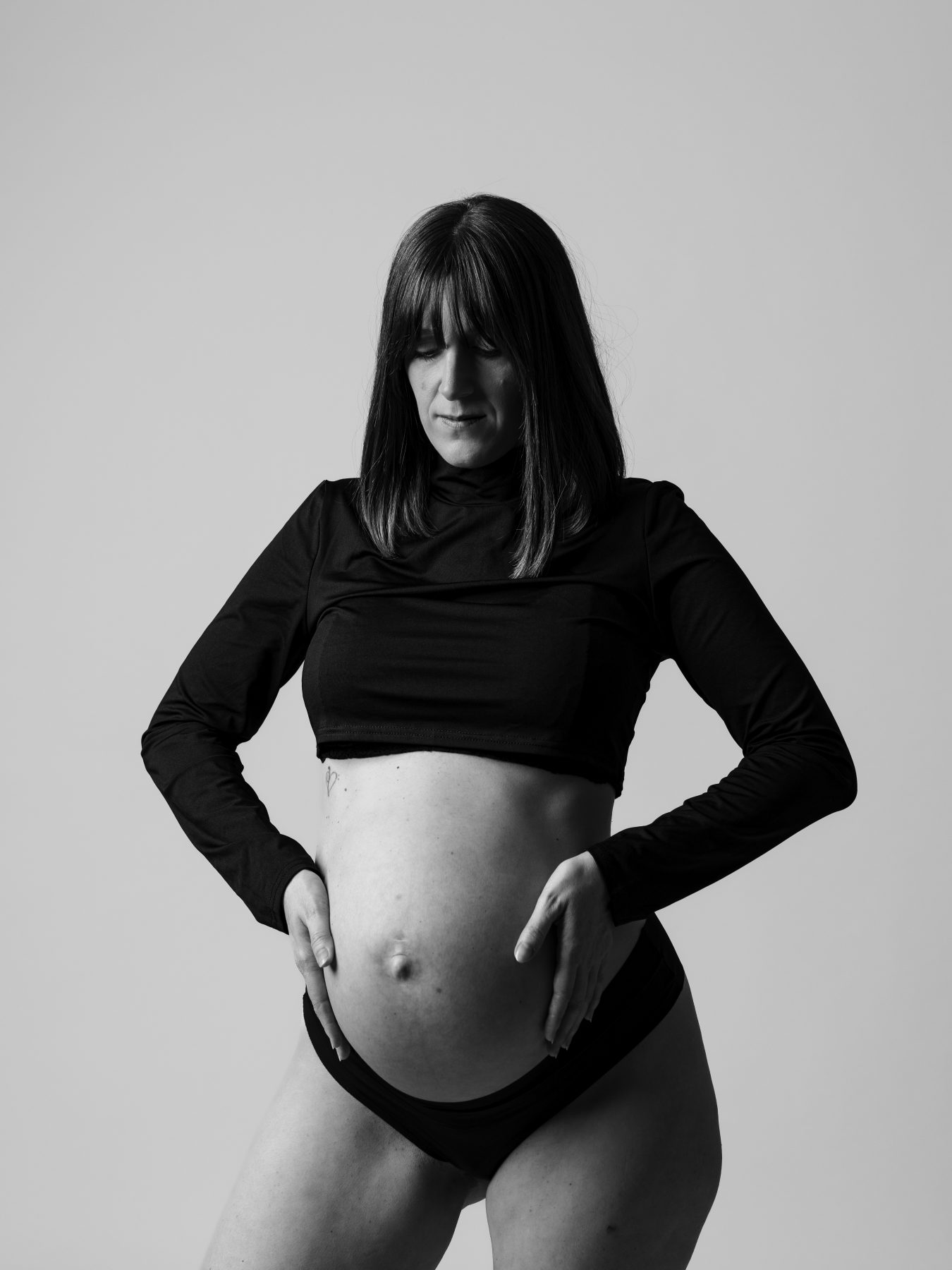 Mujer embarazada con top negro corto mostrando la barriga, blanco y negro – fotografía de maternidad por VicmanArt.