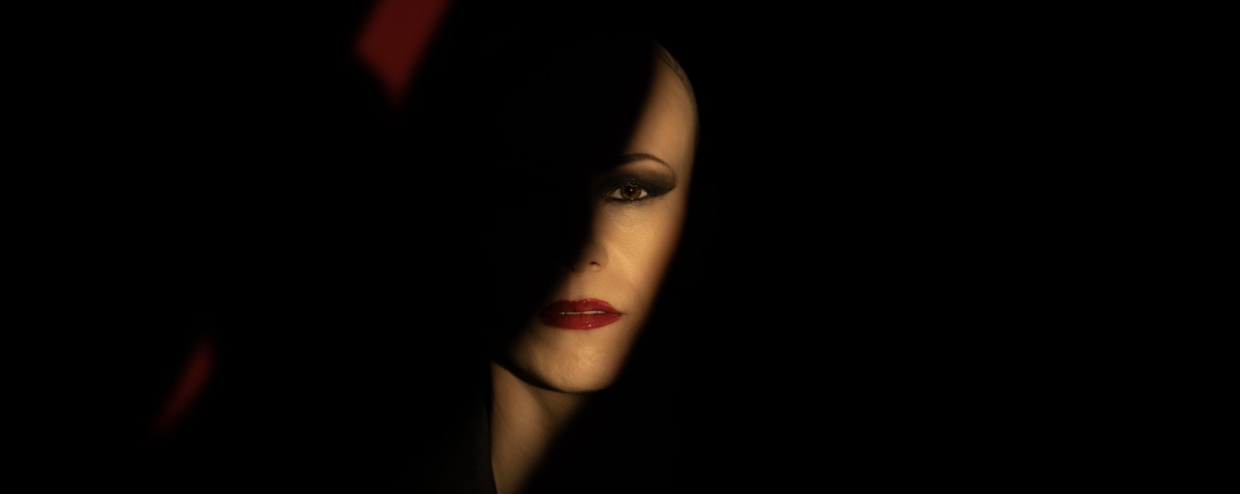 Modelo con labios rojos y ojos ahumados, media cara en sombra sobre fondo oscuro – fotografía editorial de moda por VicmanArt.