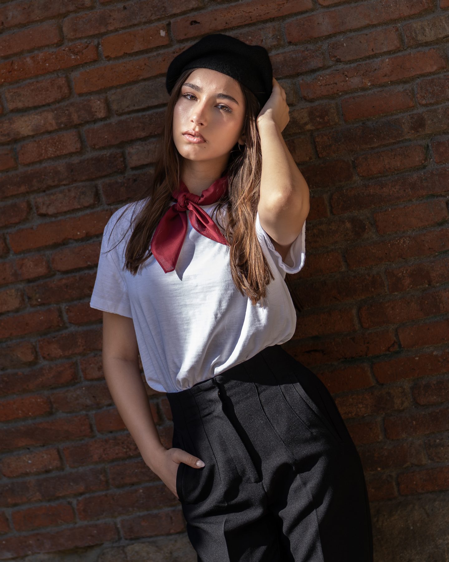 Modelo joven con boina negra y pañuelo rojo apoyada en una pared de ladrillo del Barrio Gótico de Barcelona – fotografía editorial de moda por VicmanArt.