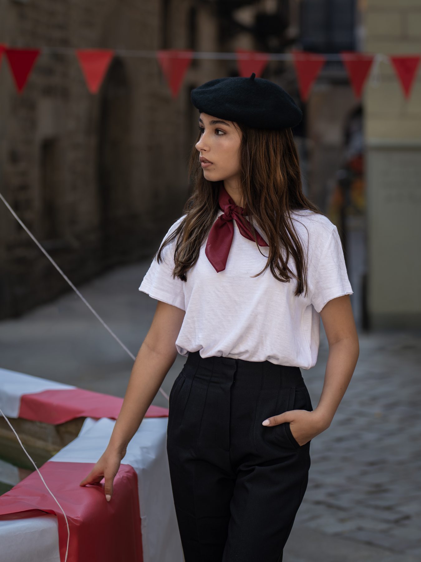 Modelo con boina negra y pañuelo rojo en una calle con banderines rojos de Barcelona – fotografía editorial de moda por VicmanArt.
