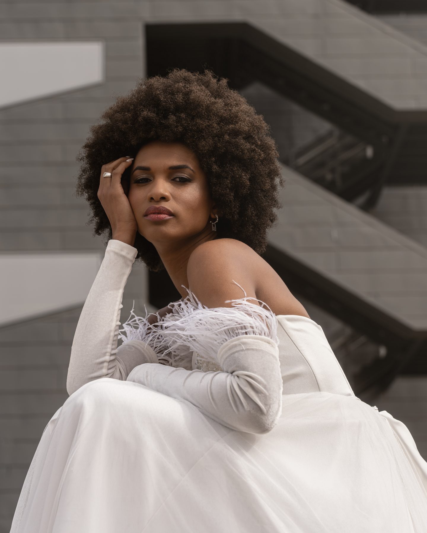 Model in a white feathered dress posing next to a modern architecture staircase in Barcelona – editorial fashion photography by VicmanArt.