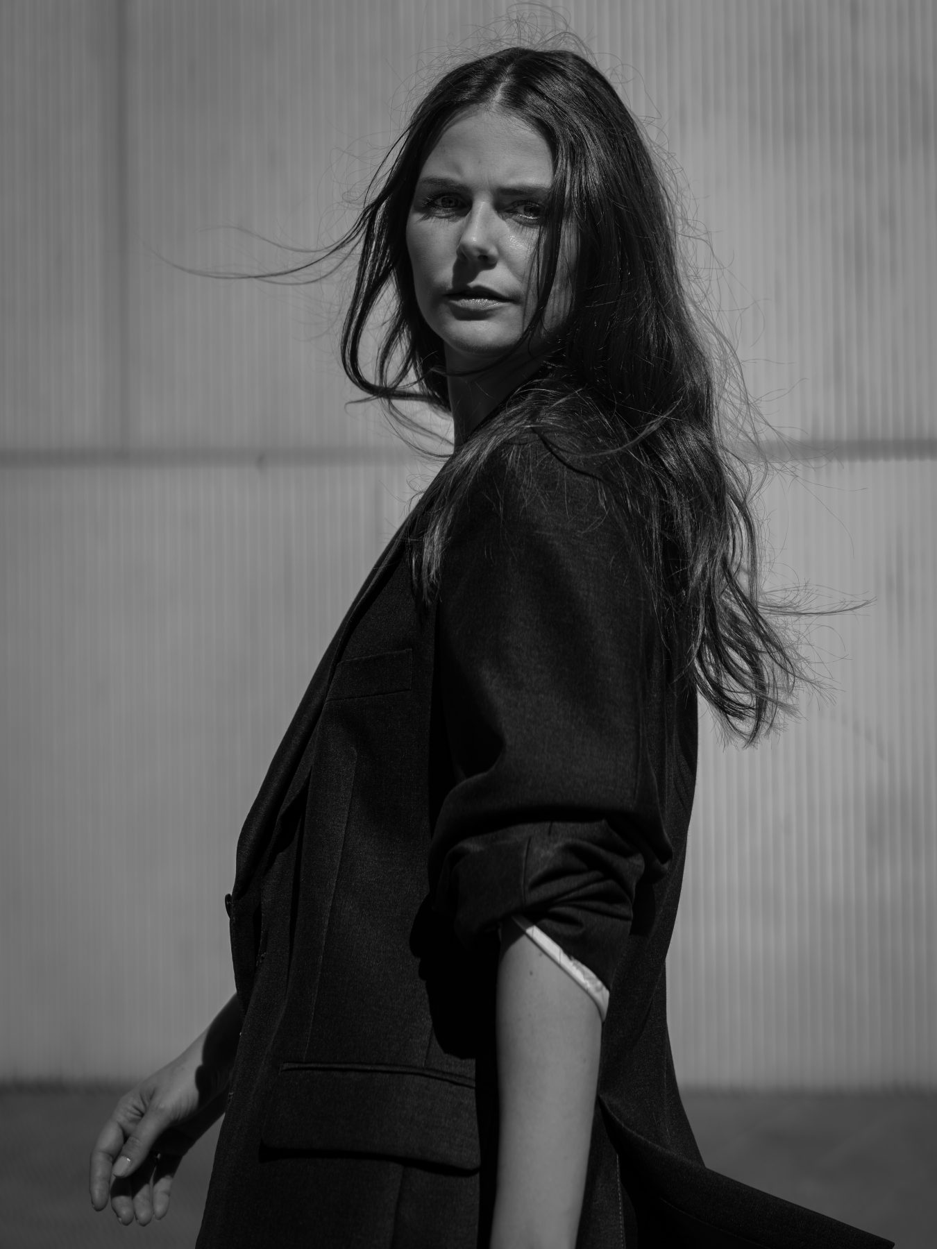 Modelo con traje negro mirando atrás de perfil con pelo al viento, blanco y negro, Barcelona – fotografía editorial de moda por VicmanArt