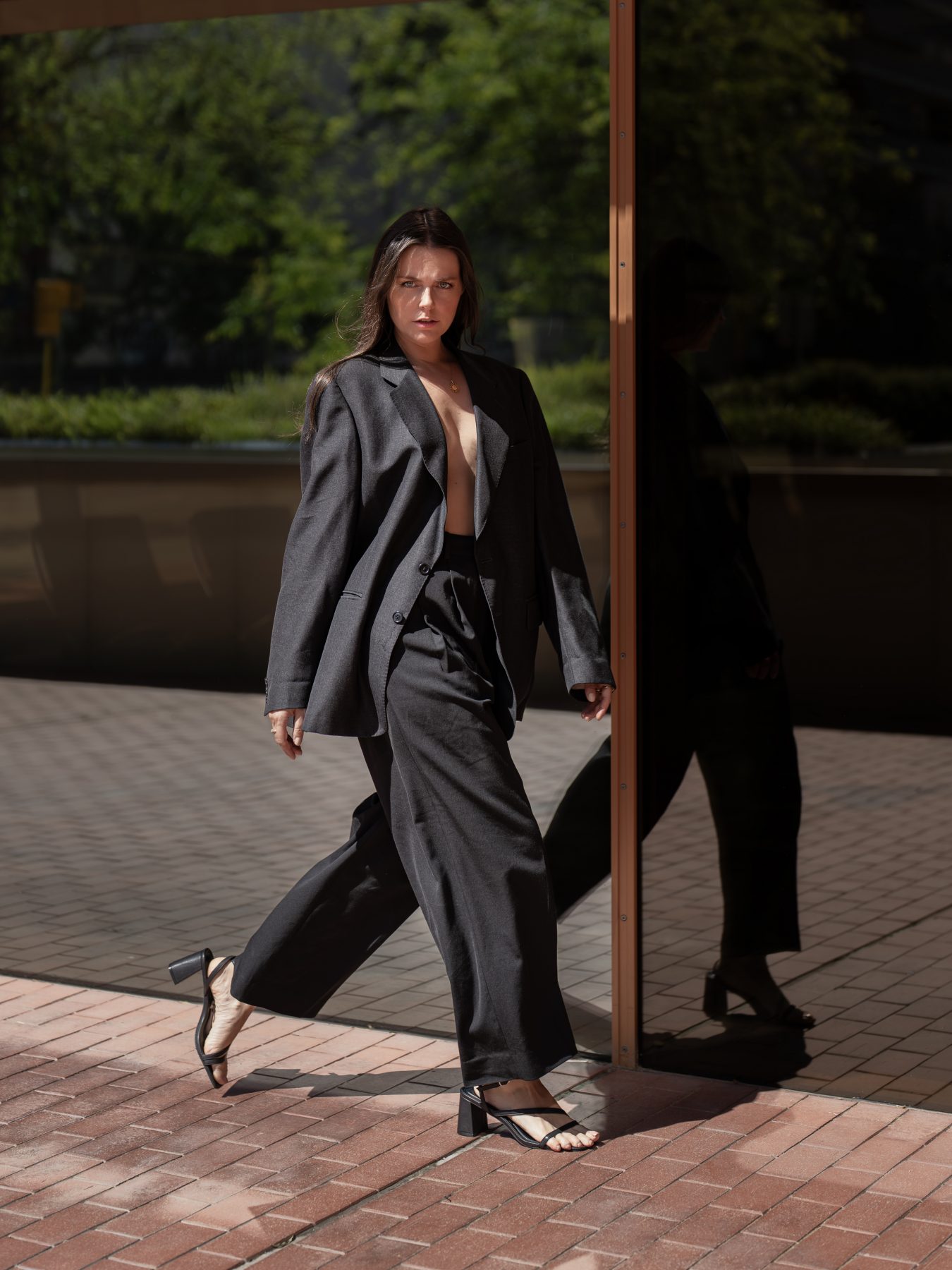 Modelo con traje gris caminando junto a su reflejo en cristal en Barcelona – fotografía editorial de moda por VicmanArt