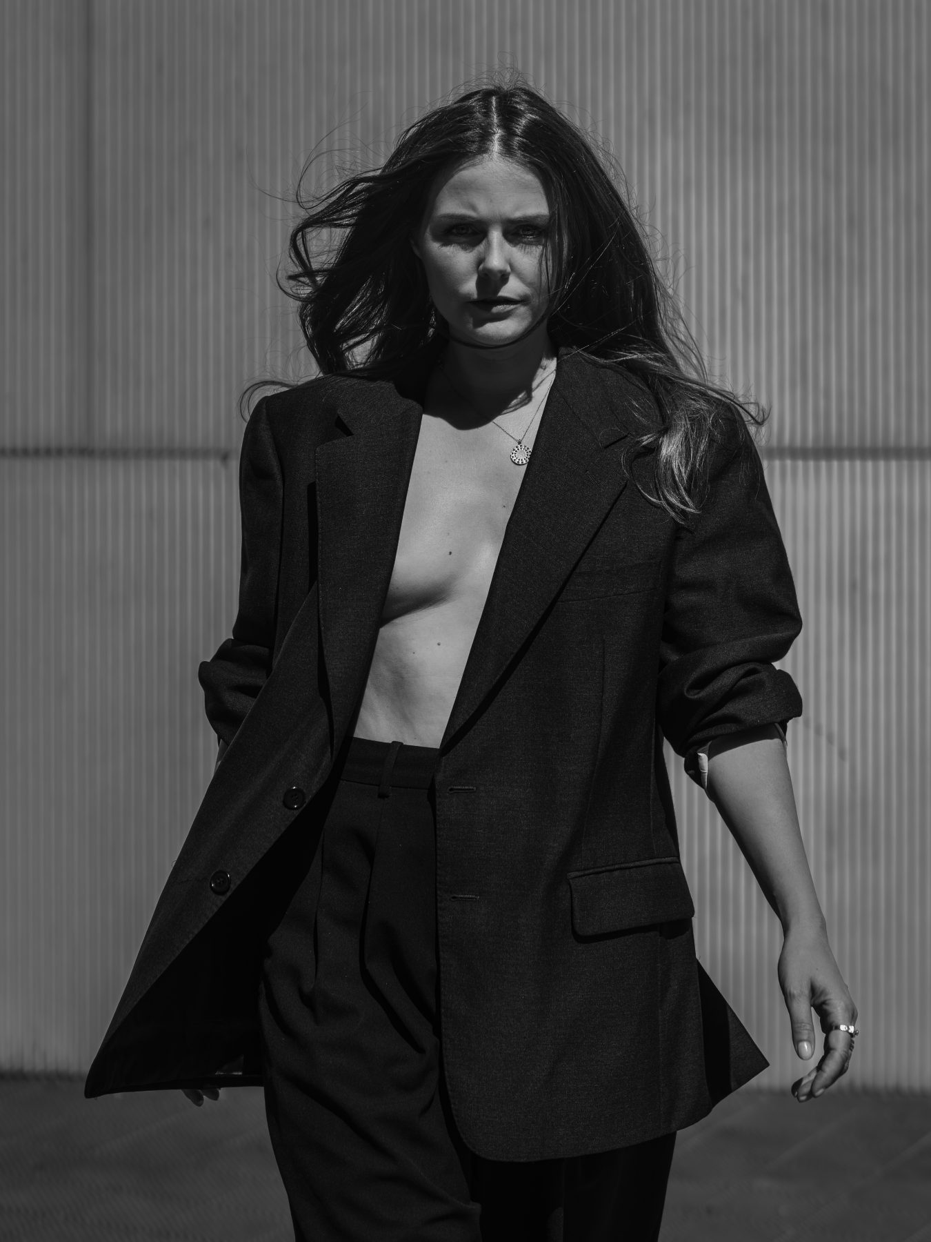 Modelo con traje negro caminando de frente con pelo al viento, blanco y negro, Barcelona – fotografía editorial de moda por VicmanArt.