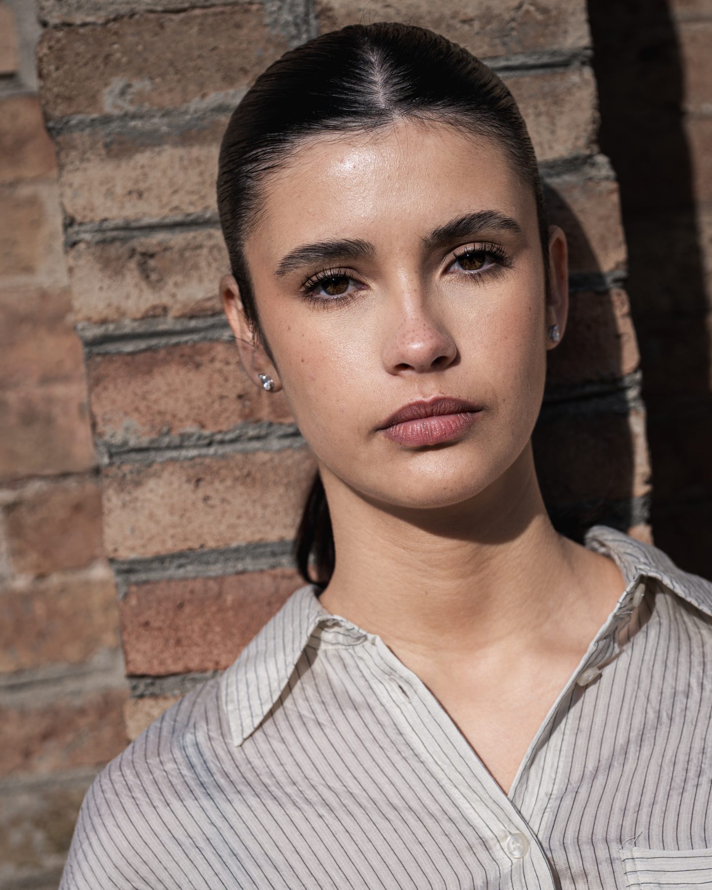 Modelo con pelo recogido y camisa de rayas frente a pared clara, primer plano en Barcelona – fotografía editorial de moda por VicmanArt