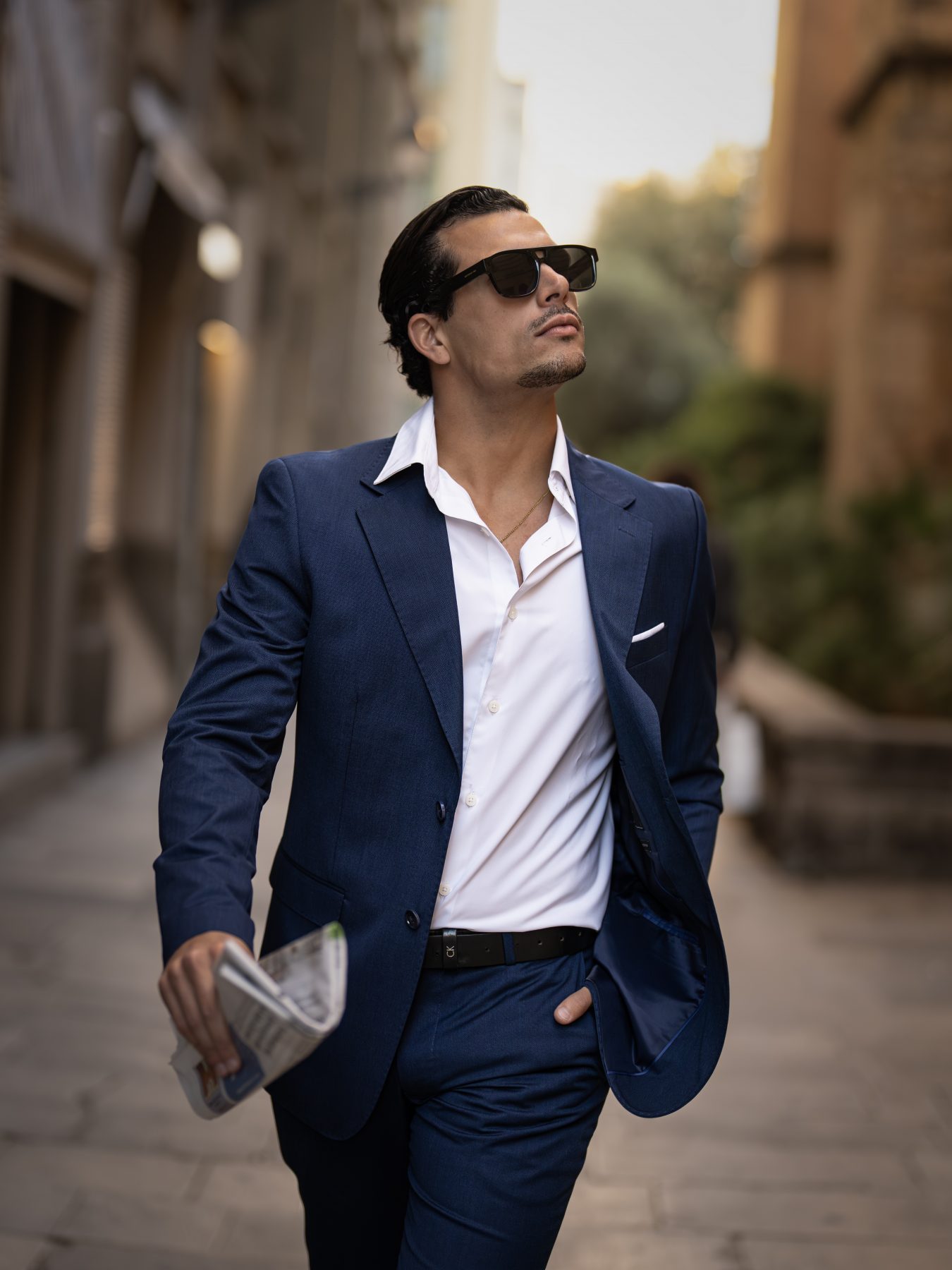 Modelo masculino con traje azul marino caminando por el casco antiguo de Barcelona – fotografía editorial de moda por VicmanArt.