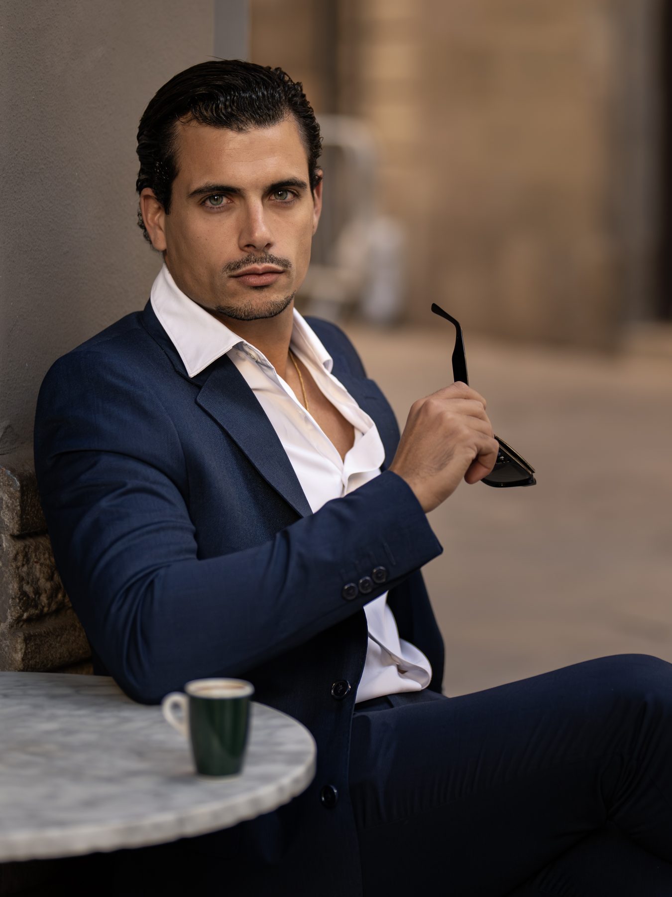Modelo masculino con traje azul marino sosteniendo las gafas de sol en una terraza, Barcelona – fotografía editorial de moda por VicmanArt.