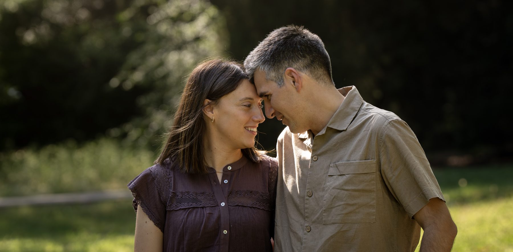 Pareja de padres con frentes juntas mirándose entre los árboles del parque, Barcelona – fotografía de familia por VicmanArt