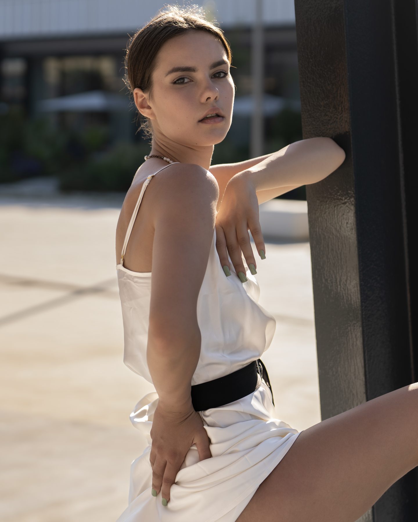 Modelo con vestido satinado blanco y cinturón negro apoyada en estructura metálica del Fòrum, Barcelona – fotografía editorial de moda por VicmanArt