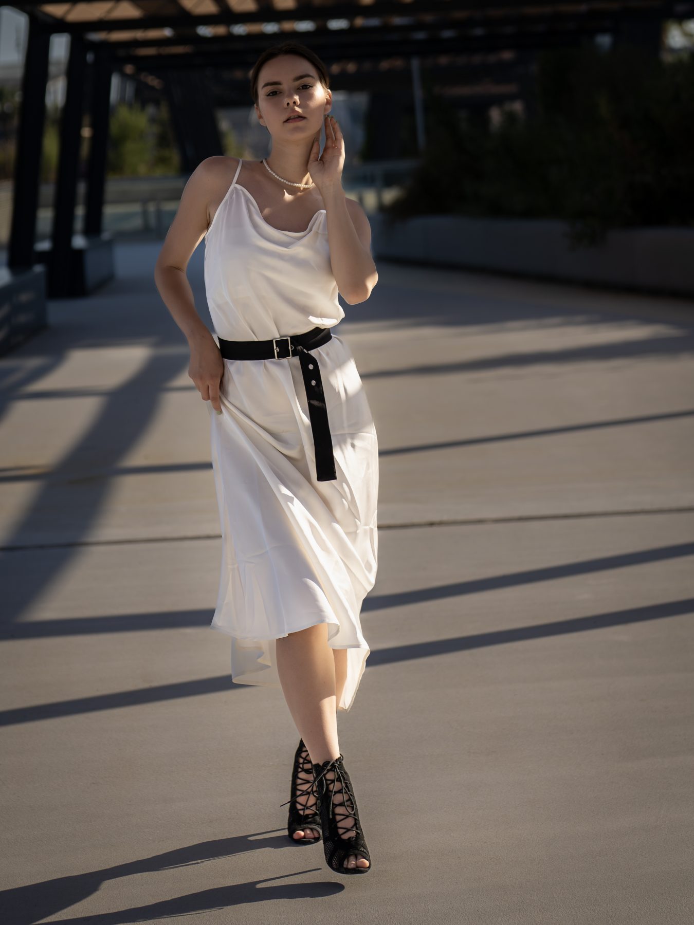 Modelo con vestido satinado blanco y cinturón negro caminando en el Fòrum de Barcelona – fotografía editorial de moda por VicmanArt